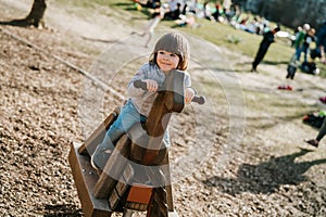 Cute happy little boy riding wooden horse toy on playground outdoors