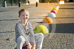 Cute happy little boy sitting on colored stones, looking at camera