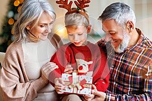 Cute happy little boy wearing reindeer antlers getting New Year present from loving grandparents