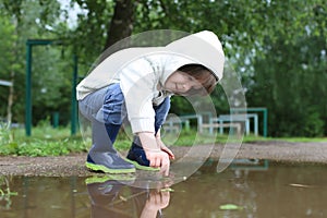 Cute happy little boy in wellingtons plays in puddle