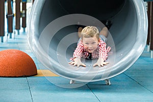 Cute happy little child boy playing in tunnel on playground. Funny kid have a fun time outdoors in park