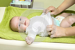 Cute happy little girl getting dressed. Mother dressing her baby on changing pad. Infant baby with diaper.