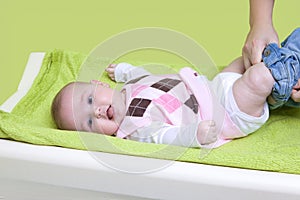 Cute happy little girl getting dressed. Mother dressing her baby on changing pad. Infant baby with pink sweater.