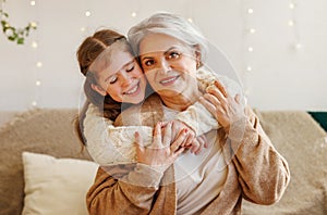 Cute happy little girl granddaughter hugging delighted elderly grandmother during Christmas holidays