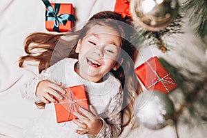 Cute happy little girl Laughing in Christmas atmosphere with gift boxes and magic lights.