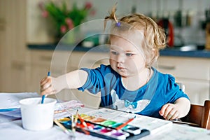 Cute happy little girl painting with water color on paper. Baby child learning different skills, creative leisure and