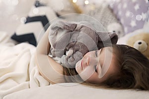 Cute happy little girl sleeping and dreaming in and bed hugging her toy. Close up photo of sleeping child