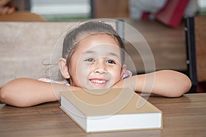 Cute happy little girl student leaning on table with book in classroom elementary school . kid or child clever sitting at desk