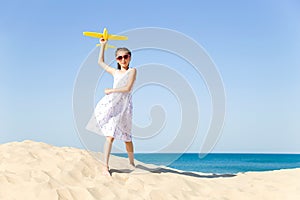 Cute happy little girl wearing sun eyeglasses and a white dress evolving in the wind playing with the yellow