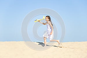 Cute happy little girl wearing a white dress running on the sandy beach by the sea and playing with the yello