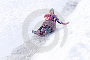 Cute happy little girls wearing a warm clothes are having fun, sliding down a hill on the ice slide