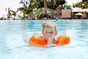 Cute happy little toddler girl swimming in the pool and having fun on family vacations in a hotel resort. Healthy child