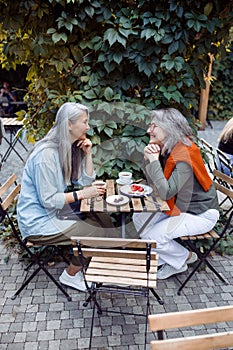 Cute happy mature women sit together on outdoors cafe terrace