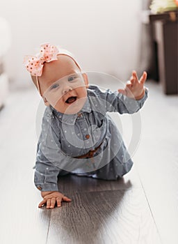 Cute happy 6 months baby girl with pink bow crawling indoor. Pretty smiling kid