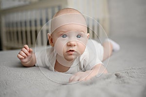 Cute happy newborn baby lies on bed on his stomach prevent colic, in background there is a crib. Portrait of a baby in a photo