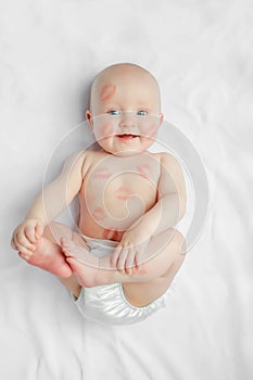 Cute happy newborn baby with red lipstick kisses on the skin sitting on white background, Valentines day concept. top