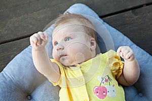 Cute happy one month baby girl in yellow clothing lying and playing