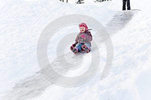 Cute happy preschool girl wearing a warm clothes is having fun, sliding down a hill on the ice slide