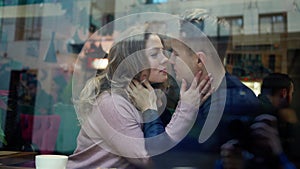 Cute Happy romantic couple embracing and kissing while sitting over the window in cafe. young man tenderly hugging and