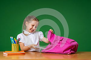 Cute happy schoolgirl puts office supplies in backpack. Preparation for school