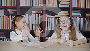 Cute happy schoolgirls sitting at desk and laughing in classroom