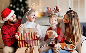 Cute happy small kids siblings getting xmas gifts while sitting with young loving parents