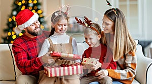 Cute happy small kids siblings getting xmas gifts while sitting with young loving parents