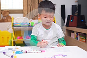 Cute happy smiling Asian 4 years old toddler boy child coloring with marker in living room at home