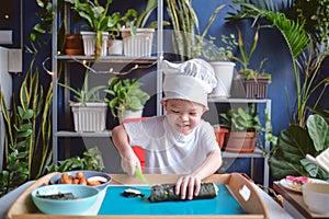 Cute happy smiling Asian little boy child wearing chef hat having fun preparing, cooking healthy Japanese food -  sushi roll at