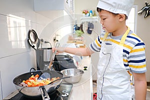 Cute happy smiling Asian boy child wearing chef hat and apron having fun preparing, cooking healthy Homemade Japanese Curry Rice