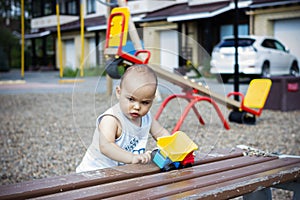 Cute happy smiling baby boy playing with colorful toy car at children playground outdoors