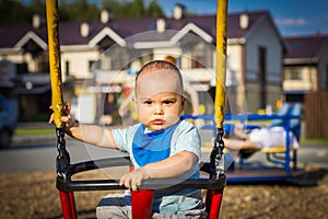 Cute happy smiling baby boy on swing at children playground outdoors