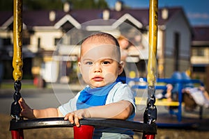 Cute happy smiling baby boy on swing at children playground outdoors