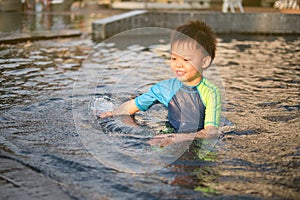 Cute happy smiling little Asian boy child in swimming suit enjoy playing at swimming pool in sunny summer day, Happy kid having