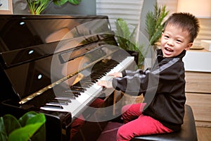 Cute happy smiling little Asian kid boy playing piano in living room, Preschool child having fun with learning to play music