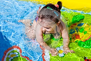 Cute, happy, smiling toddler baby girl, swimming, and playing in colorful inflatable