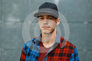 Cute happy stylish young man in a colorful vintage checkered shirt in a fashionable black basketball cap in a t-shirt