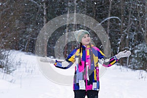Cute happy teenage girl is catching snowflakes with her hands in winter