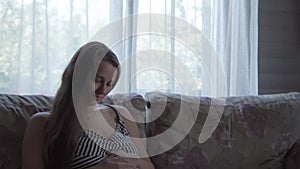 cute happy tired pregnant woman touching her tummy resting sitting in bed at home. caring mother take rest stroke belly