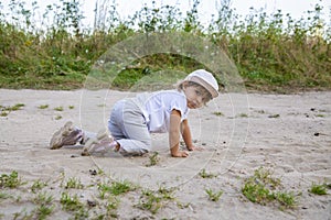 Cute happy toddler in a cap crawls on all fours along a country road in the sand on a sunny summer day