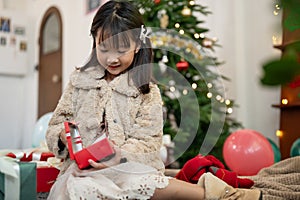 A cute and happy young Asian girl is opening a Christmas gift in the living room