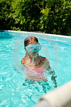A cute happy young girl child playing in swimming pool wearing blue diving mask