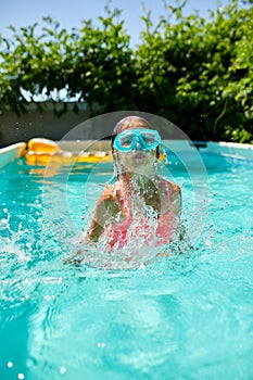 A cute happy young girl child playing in swimming pool wearing blue diving mask