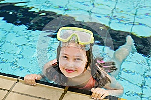 Cute happy young girl in goggles swimming and snorking in the swimming pool. Happy child in summer in outdoor pool