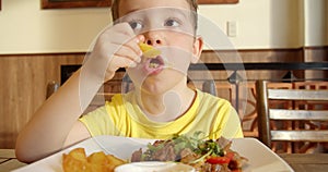 Cute healthy preschool boy eating potatoes and bell peppers,vegetables cooked on a barbecue,sitting in children's cafe