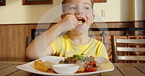 Cute healthy preschool boy eating potatoes and bell peppers,vegetables cooked on a barbecue,sitting in children's cafe