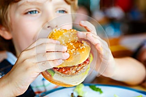 Cute healthy preschool boy eats hamburger sitting in cafe outdoors