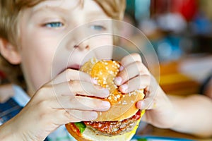 Cute healthy preschool boy eats hamburger sitting in school canteen