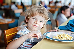Cute healthy preschool boy eats pasta sitting in school canteen