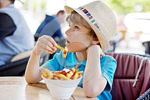 Cute healthy preschool kid boy eats french fries potatoes with ketchup